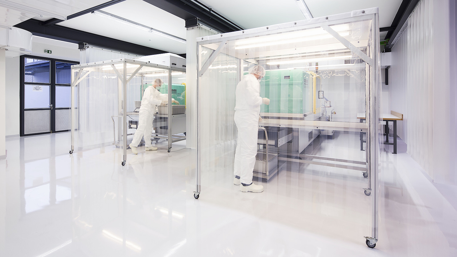 Das Bild zeigt zwei 1zu1mitarbeiter in Schutzkleidung in der 1zu1reinraumfertigung für die Herstellung von keimfreien und sterilen Kunststoffteilen.