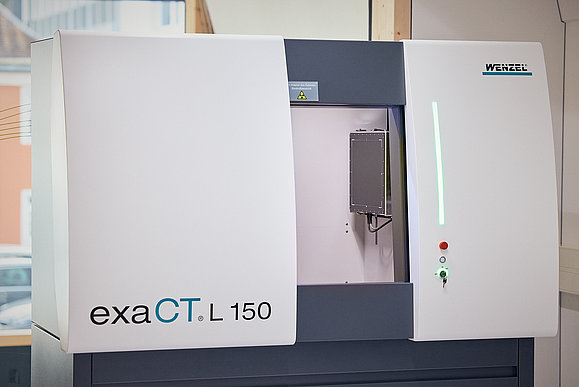 Das Bild zeigt das Innenleben des neuesten Computertomographen exaCT L 150 mit geöffneter Türe und Ansicht auf die Messplatte.