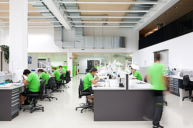 Das Bild zeigt die 1zu1 Vakuumguss Produktionshalle mit Mitarbeiterin in der grünen Arbeitskleidung beim Finish von diversen Kundenprojekten.